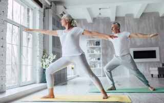Senior couple doing yoga in living room near window