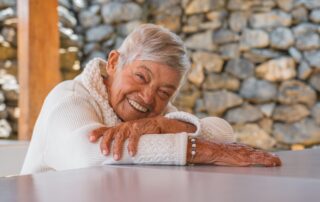 Happy senior woman outside smiling with her head resting on her arms who is enjoying her time at retirement communities